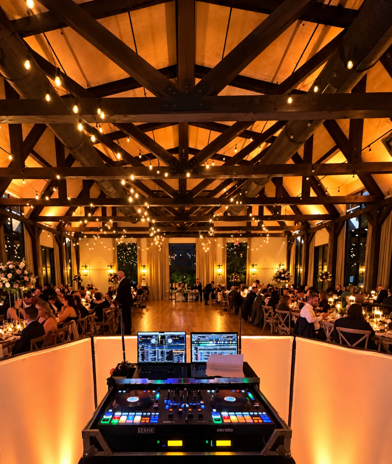 View from the Westchester Entertainment DJ setup across the wedding reception room at The Barn at Villa Venezia, showing its wooden beams, long room and guests seated for dinner